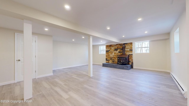 basement with light wood finished floors, a baseboard radiator, a wood stove, and recessed lighting