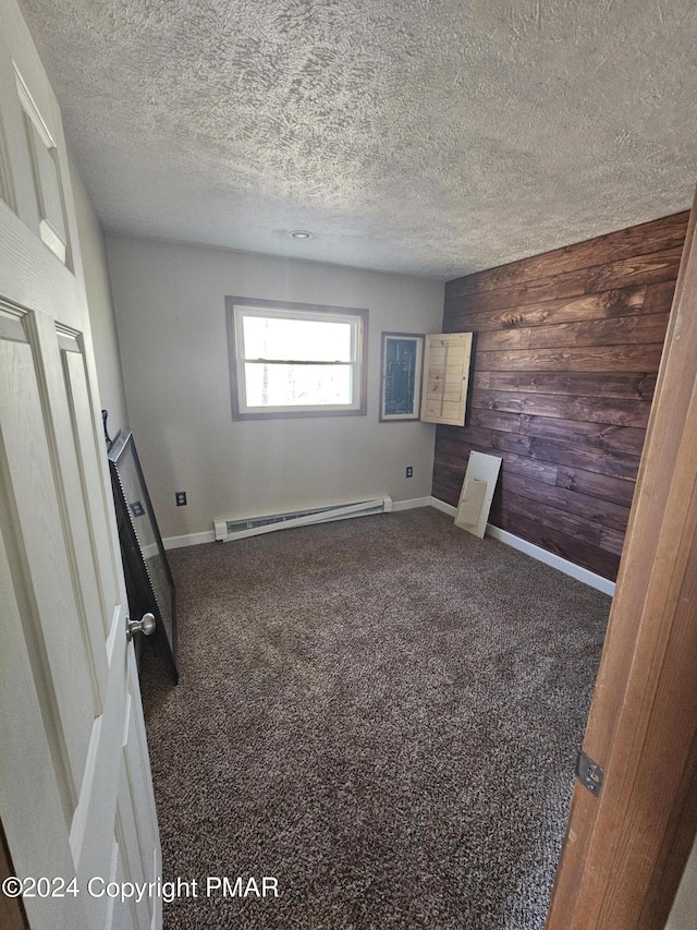 unfurnished bedroom with baseboards, wood walls, carpet flooring, a textured ceiling, and a baseboard radiator