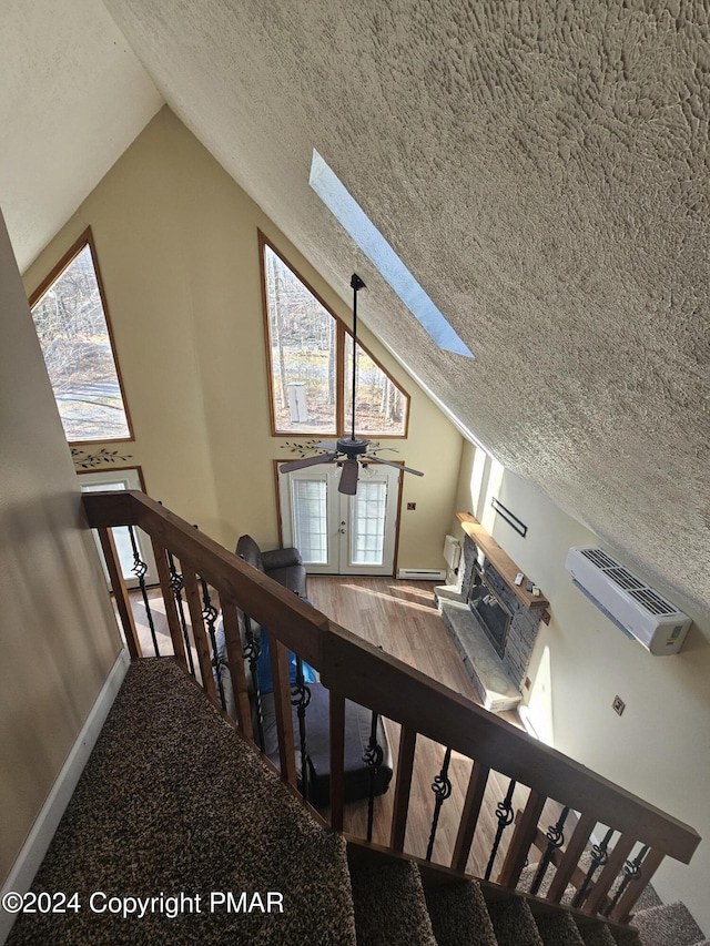 staircase featuring a ceiling fan, vaulted ceiling with skylight, a fireplace with raised hearth, and a textured ceiling