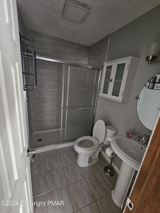 bathroom with a sink, toilet, a stall shower, and a textured ceiling