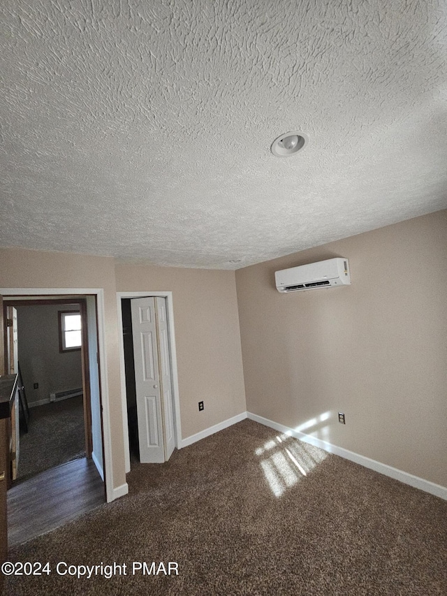 empty room with a textured ceiling, a wall unit AC, dark colored carpet, a baseboard radiator, and baseboards