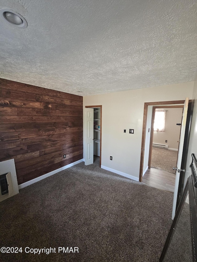 unfurnished bedroom featuring wooden walls, baseboards, carpet flooring, a closet, and a textured ceiling