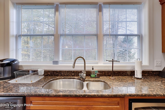 details with beverage cooler, a sink, brown cabinets, dishwasher, and dark stone countertops