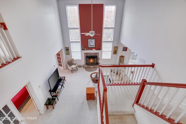 interior space featuring a warm lit fireplace, stairs, a high ceiling, and a ceiling fan