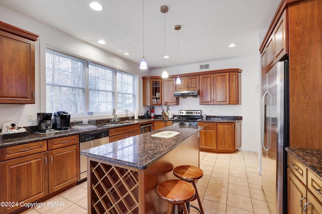 kitchen with a breakfast bar, stainless steel appliances, under cabinet range hood, a sink, and light tile patterned flooring