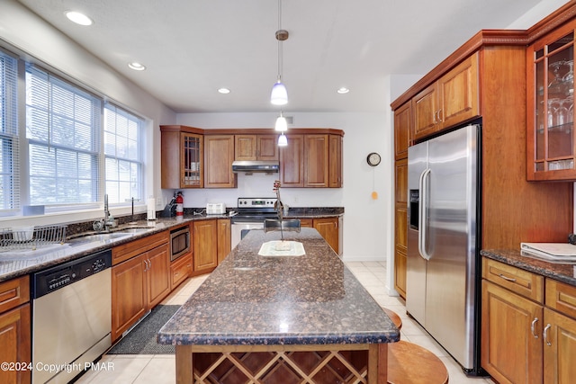 kitchen with light tile patterned flooring, under cabinet range hood, stainless steel appliances, a sink, and brown cabinets