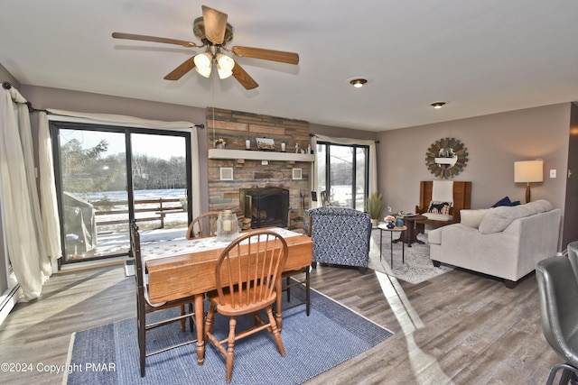 dining room with a stone fireplace, a ceiling fan, and wood finished floors