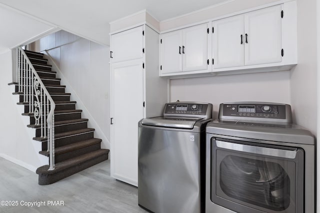 clothes washing area featuring cabinet space, washing machine and clothes dryer, and wood finished floors