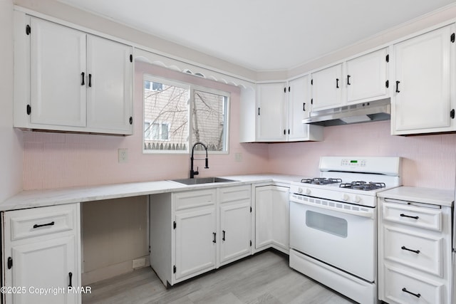 kitchen with tasteful backsplash, white cabinets, gas range gas stove, under cabinet range hood, and a sink