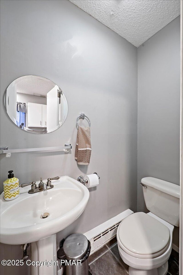 half bathroom featuring toilet, a baseboard heating unit, a sink, a textured ceiling, and tile patterned flooring