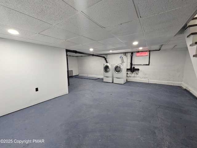 finished basement with a paneled ceiling, washing machine and clothes dryer, concrete block wall, and recessed lighting