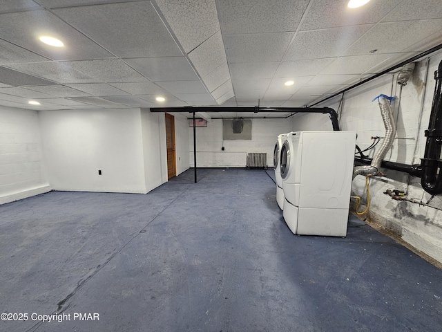 finished basement with concrete block wall, a paneled ceiling, washer and clothes dryer, and radiator heating unit