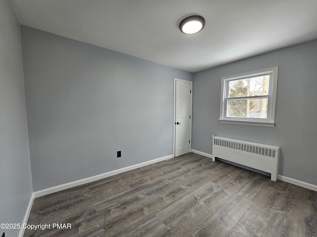 spare room featuring baseboards, wood finished floors, and radiator