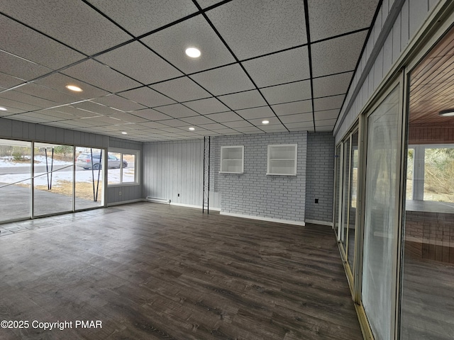 unfurnished room with recessed lighting, brick wall, wood finished floors, a drop ceiling, and baseboards