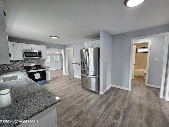 kitchen with stainless steel appliances, dark stone countertops, wood finished floors, and white cabinetry