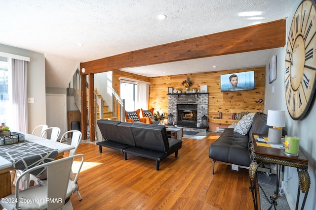 living room with stairway, a brick fireplace, wood walls, and wood finished floors