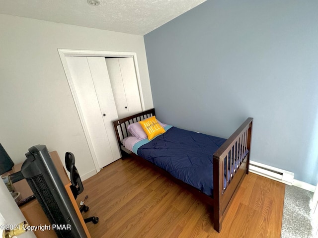 bedroom featuring baseboard heating, a textured ceiling, baseboards, wood finished floors, and a closet