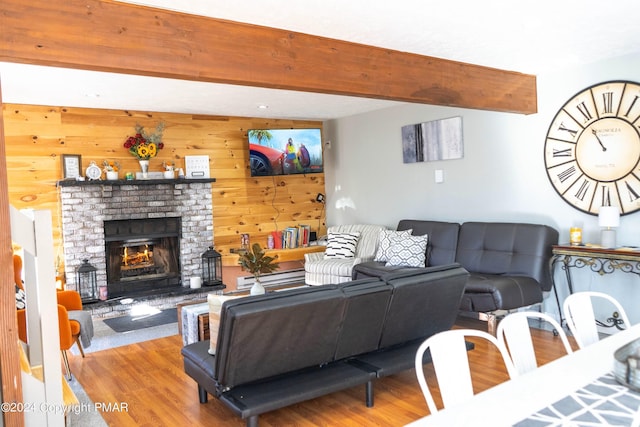 living room featuring beamed ceiling, a fireplace, wood walls, and wood finished floors