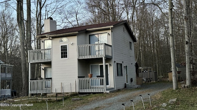 exterior space featuring a balcony, driveway, a chimney, a storage unit, and an outbuilding