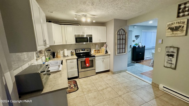 kitchen with light countertops, white cabinets, appliances with stainless steel finishes, and baseboard heating