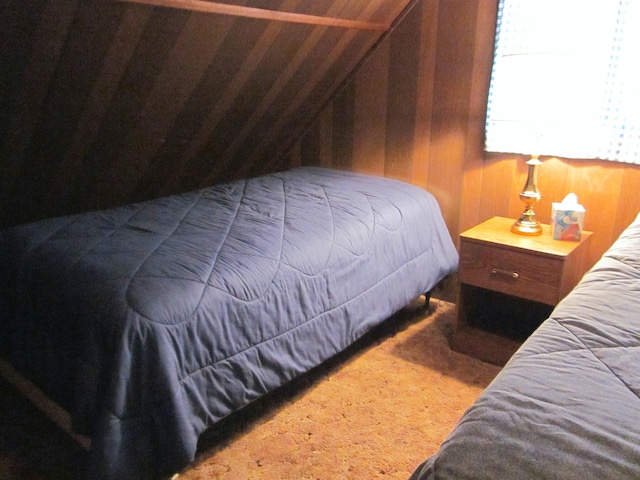 carpeted bedroom featuring wooden walls and vaulted ceiling