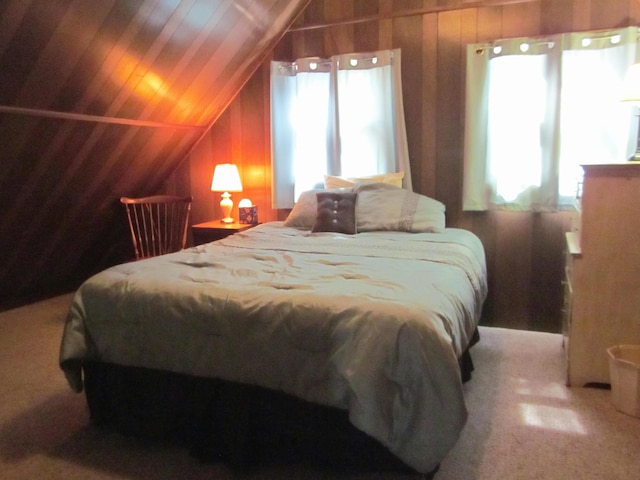 carpeted bedroom featuring wooden walls, vaulted ceiling, and multiple windows