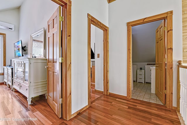 corridor with vaulted ceiling, a wall unit AC, and light wood-type flooring