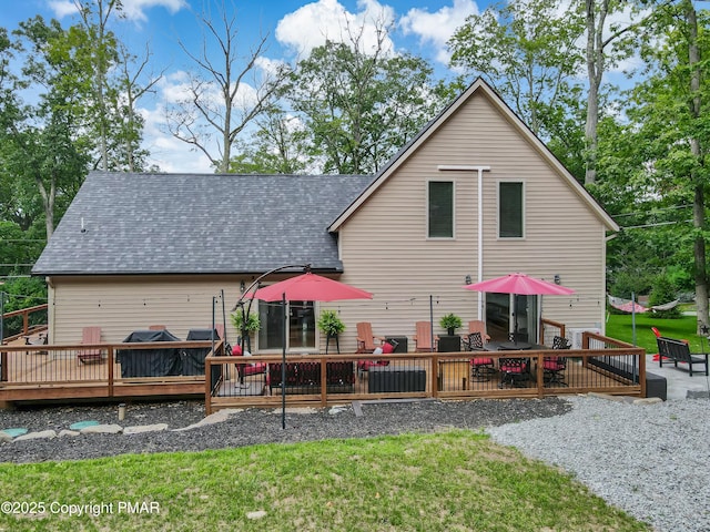 back of house with roof with shingles, a lawn, and a wooden deck