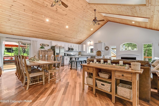 dining space with a fireplace, light wood-style flooring, wood ceiling, ceiling fan, and high vaulted ceiling