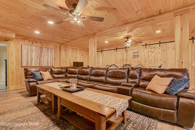 living area with a barn door, a ceiling fan, wood ceiling, wood walls, and wood finished floors