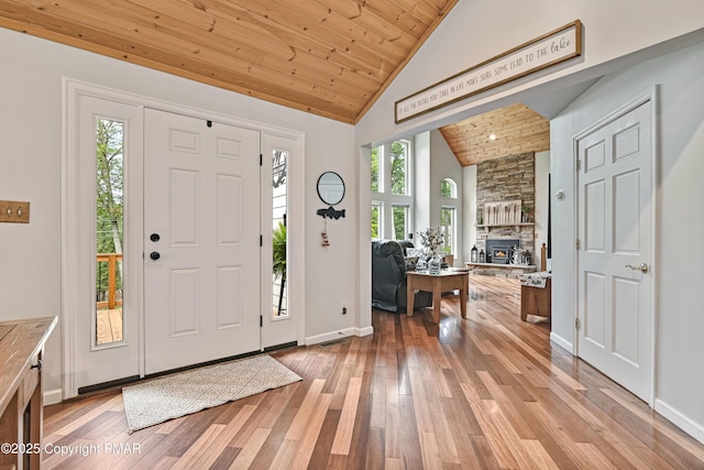 foyer entrance featuring a fireplace, light wood-style flooring, wood ceiling, high vaulted ceiling, and baseboards