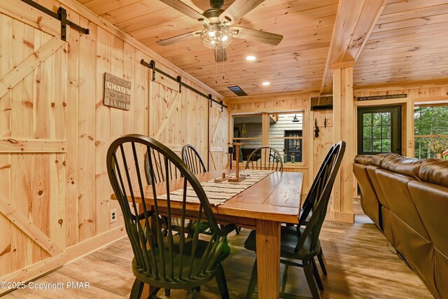 dining space with wooden ceiling, a barn door, light hardwood / wood-style flooring, and wood walls