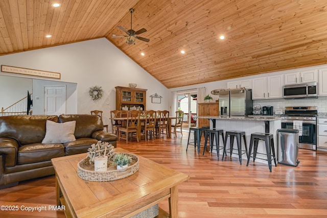 living area featuring ceiling fan, wood ceiling, light wood-style flooring, stairs, and high vaulted ceiling