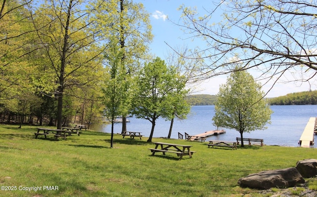 view of community with a boat dock, a water view, and a lawn