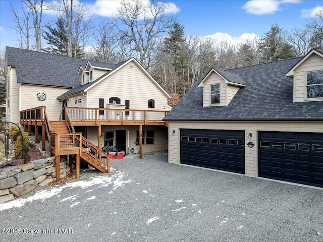 view of front of property featuring driveway, stairway, roof with shingles, an attached garage, and a deck