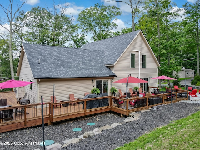 back of property with roof with shingles, outdoor dining area, and a wooden deck