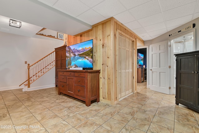 interior space with a drop ceiling, wooden walls, baseboards, and stairs