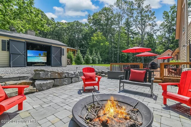 view of patio / terrace featuring a wooden deck, an outbuilding, and an outdoor fire pit