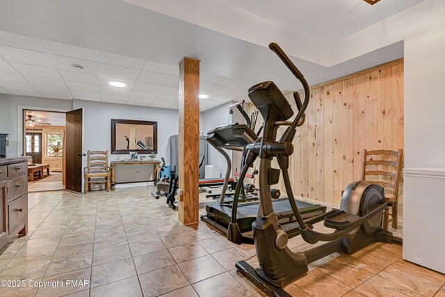 exercise room featuring wooden walls and a drop ceiling