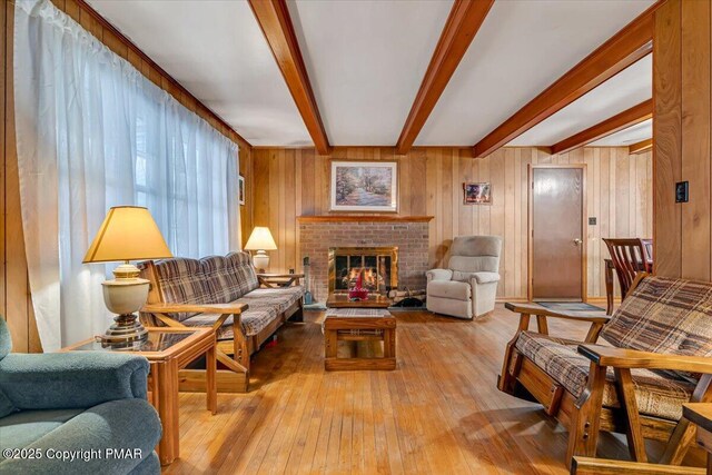 living room with beamed ceiling, wooden walls, a fireplace, and light hardwood / wood-style flooring