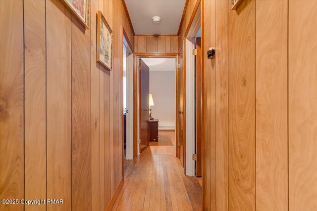 corridor with light hardwood / wood-style floors and wood walls