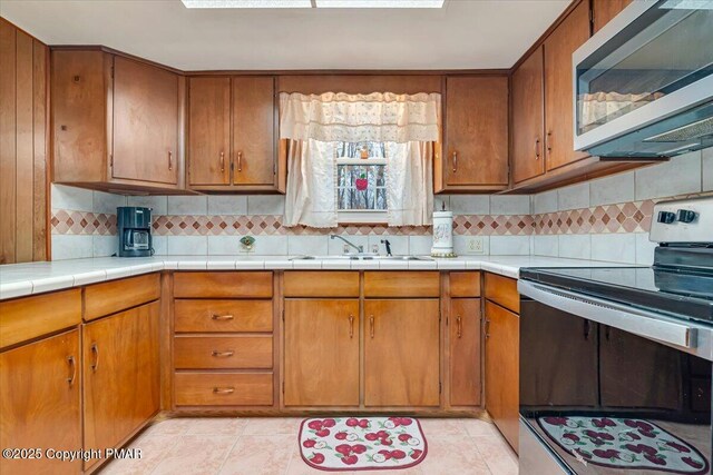 kitchen with light tile patterned flooring, appliances with stainless steel finishes, tasteful backsplash, sink, and tile counters