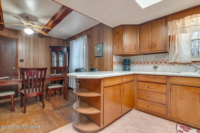 kitchen featuring wood walls, sink, decorative backsplash, tile counters, and ceiling fan