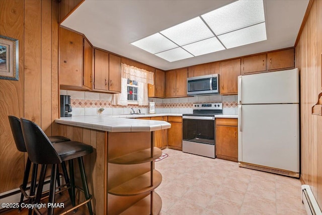 kitchen with appliances with stainless steel finishes, a baseboard radiator, sink, backsplash, and tile counters