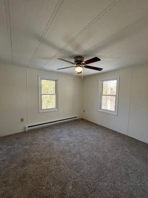 empty room featuring a wealth of natural light, baseboard heating, and carpet flooring