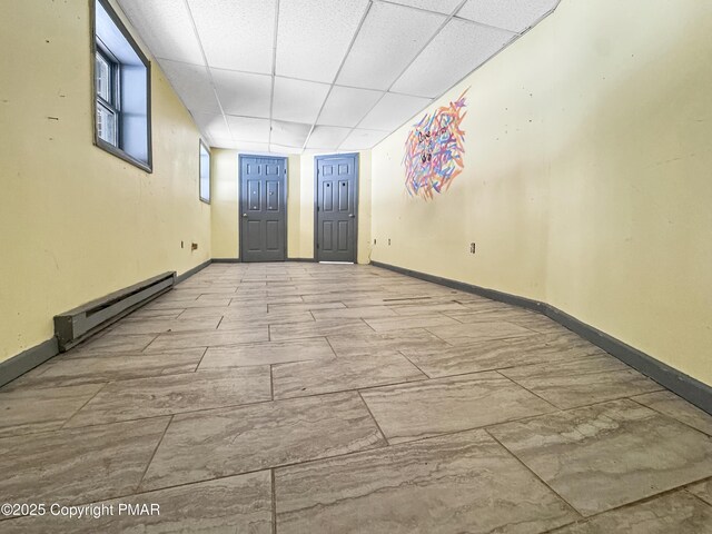 empty room with a baseboard heating unit, a drop ceiling, and baseboards