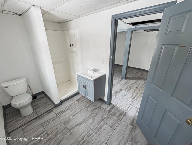 bathroom featuring a drop ceiling, toilet, vanity, baseboards, and a stall shower