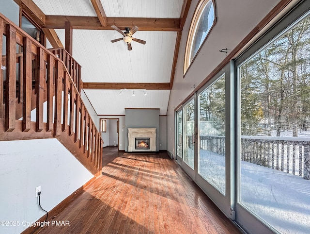 unfurnished living room featuring beam ceiling, hardwood / wood-style flooring, a glass covered fireplace, high vaulted ceiling, and stairs