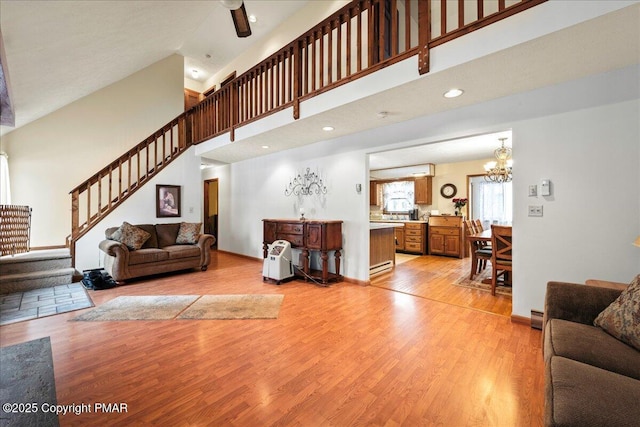 living room with baseboards, stairs, a high ceiling, light wood-type flooring, and a notable chandelier