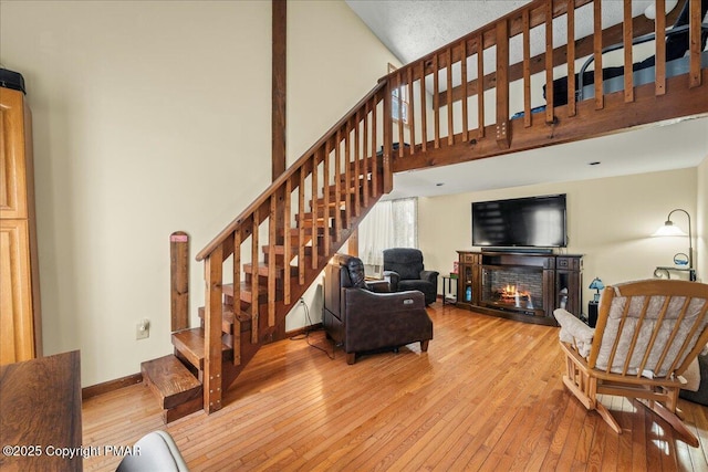 living area with a warm lit fireplace, baseboards, a towering ceiling, light wood-style flooring, and stairway